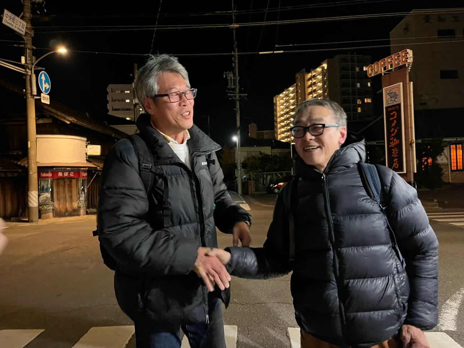 夜の街角で握手する渡辺英司と渡辺英治